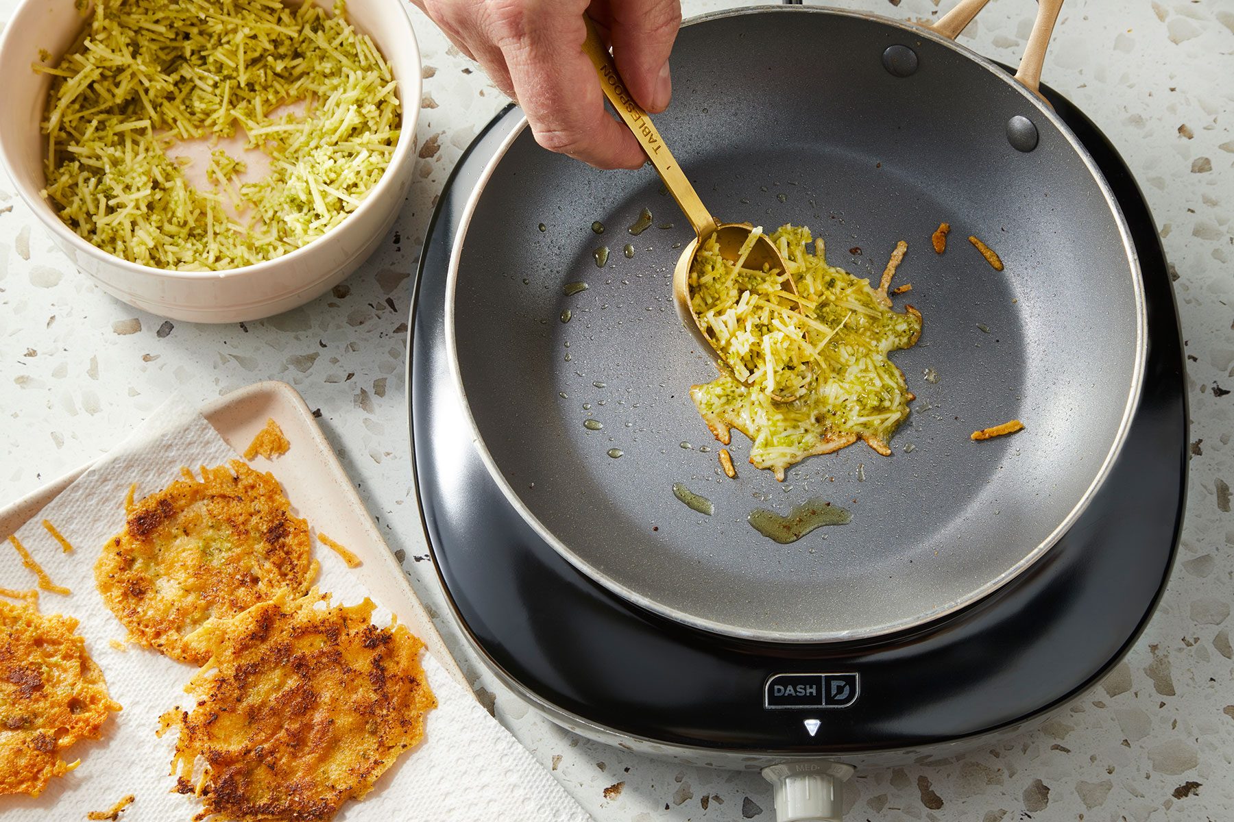A small batch of pesto-cheese mixture spread out in an even layer into a large nonstick skillet. A cooked batch on side.