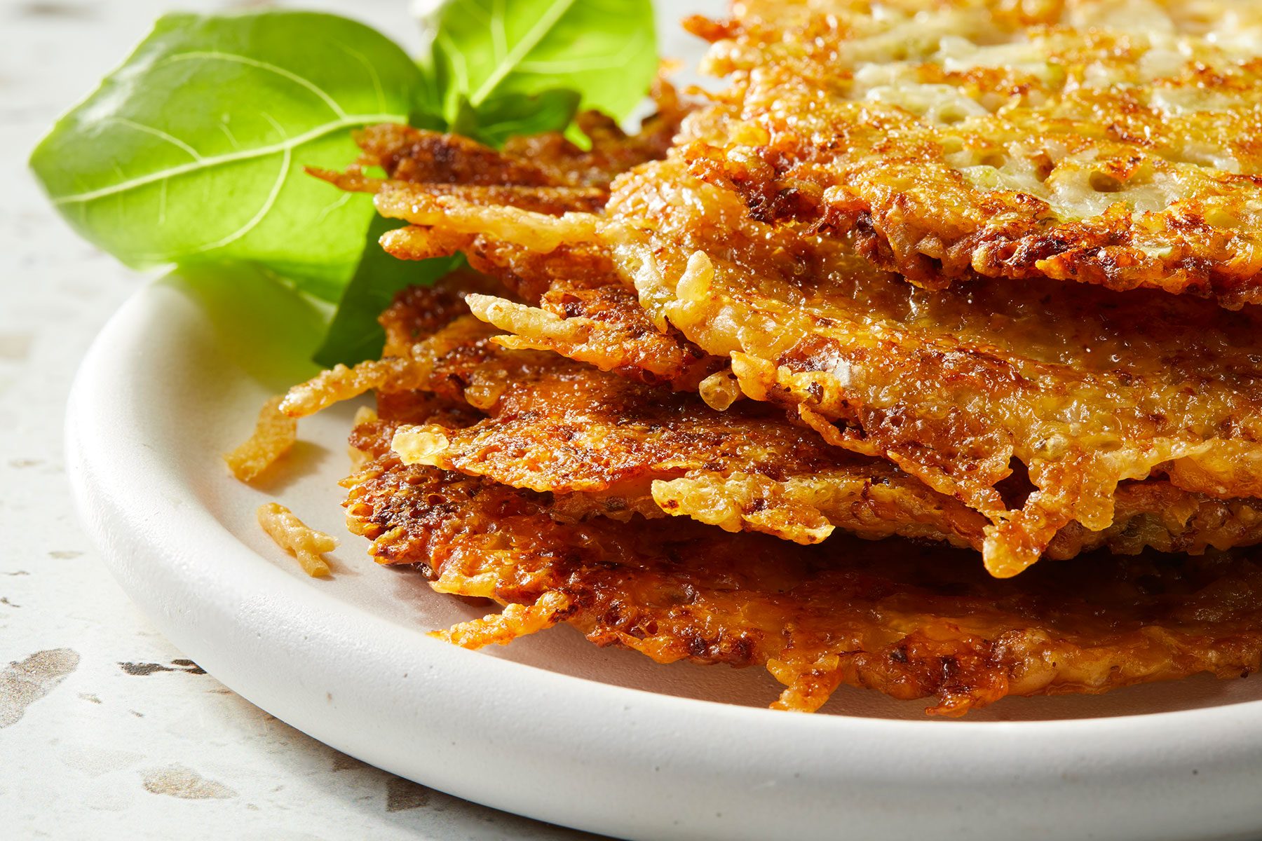 Pesto Parmesan Crisps placed in a pile on a white plate with some green garnishing on side.