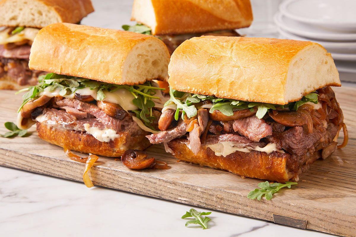 3/4 angle horizontal image of multiple prime rib sandwiches served on a wooden board.