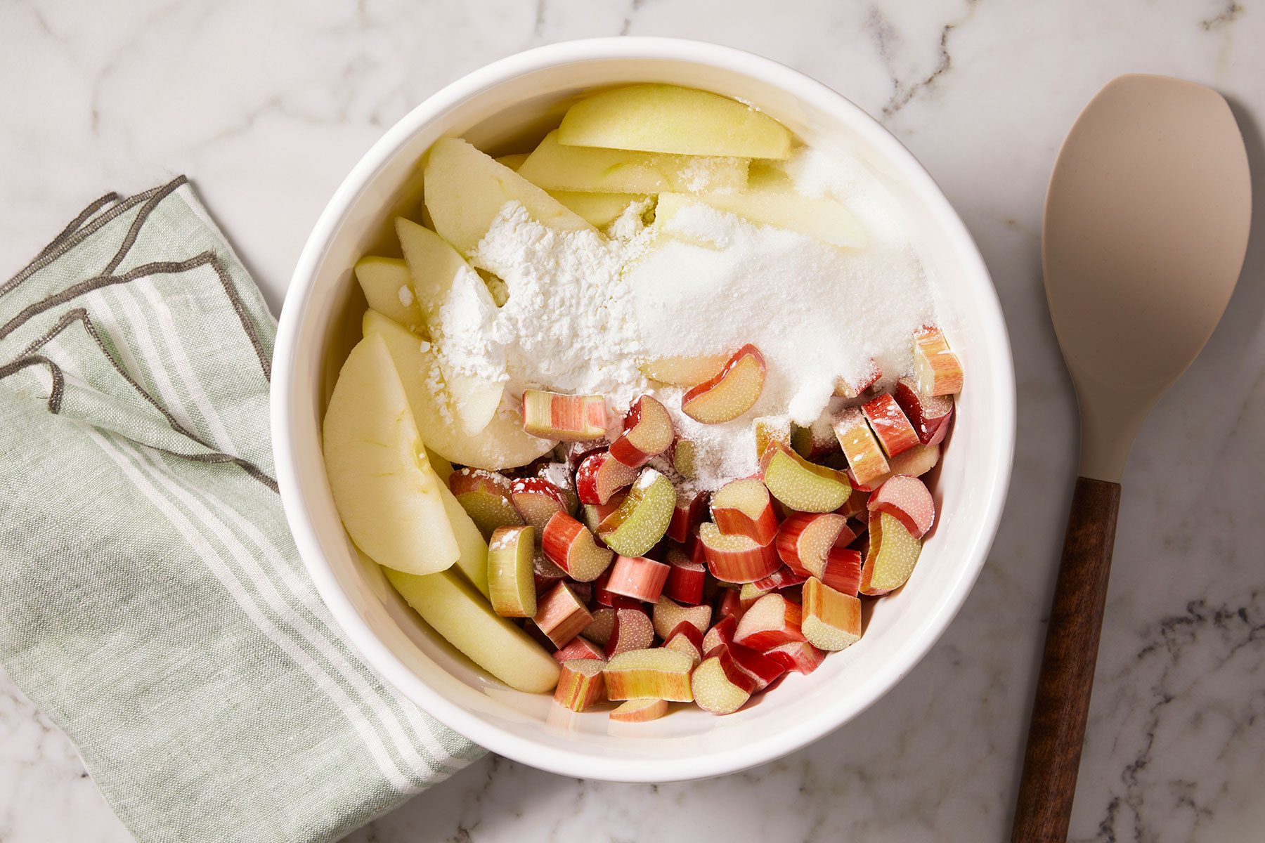 Chopped rhubarb and apples with cornstarch and sugar in a large white bowls.