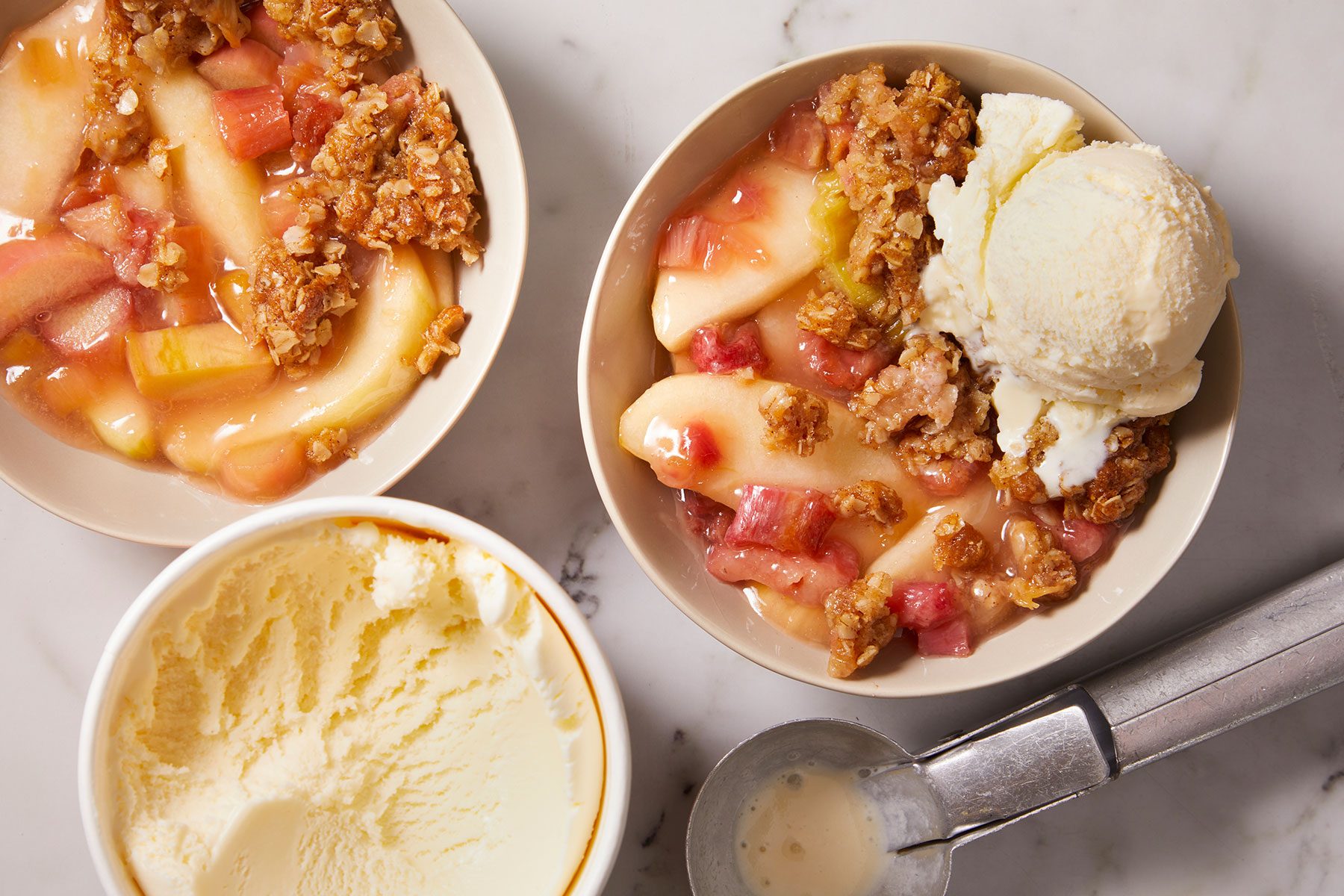 Warm Rhubarb Crisp recipe with a scoop of vanilla ice cream in a white bowl with more ice cream being kept on side.