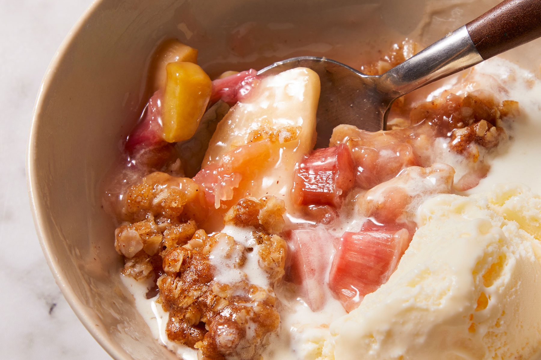 Warm Rhubarb Crisp with ice cream in a bowl with a spoon inside it.