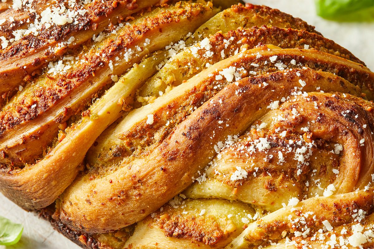 Eye Level horizontal image of a braided loaf, glistening with pesto, garlic, and parmesan. The loaf is golden brown and sprinkled with grated cheese. | [Original] RMS 282446 Savory Babka with Pesto; Horizontal; Push