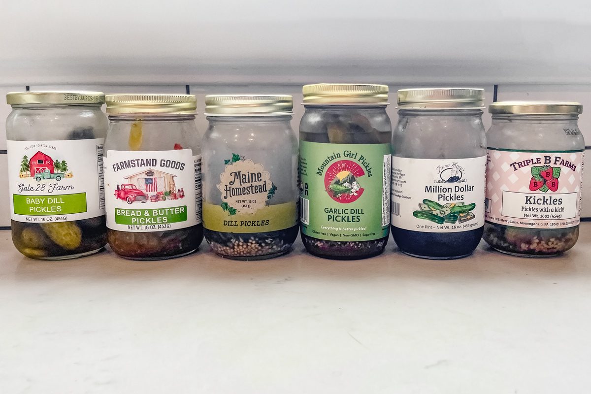 six jars of pickle on a kitchen counter