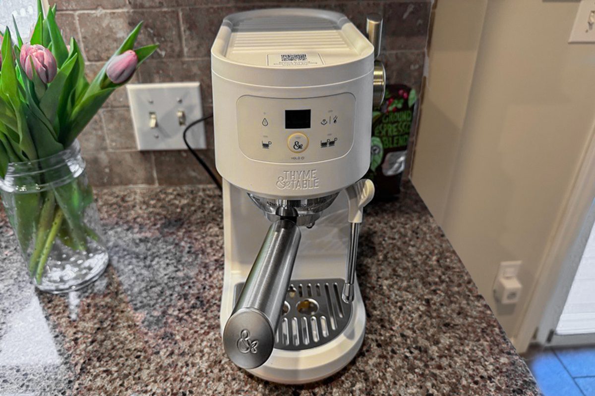 A white espresso machine sits on a granite kitchen countertop near a vase of pink tulips and a wall outlet.