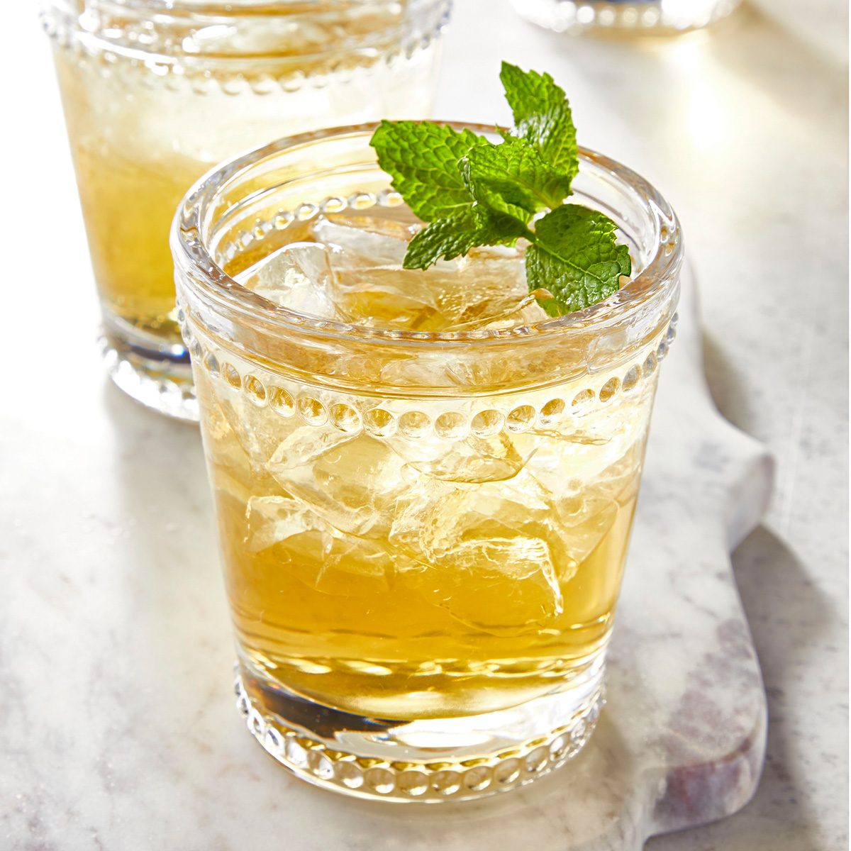 3/4th shot; white textured background; mint julep served in three glasses; garnishned with mint leaves;