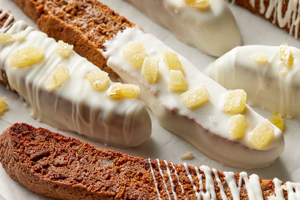 Eye Level horizontal image of biscotti being decorated. The biscotti is dipped in white chocolate and topped with candied ginger.