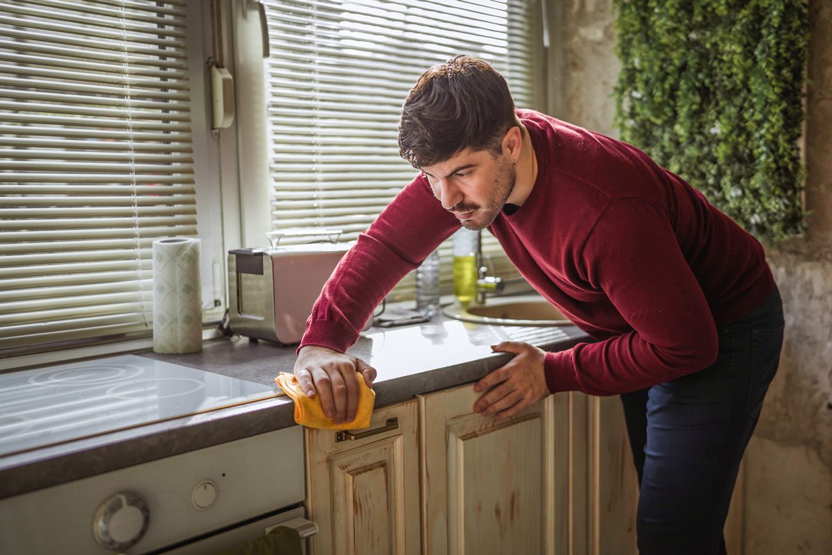 man wiping kitchen counter with yellow cloth