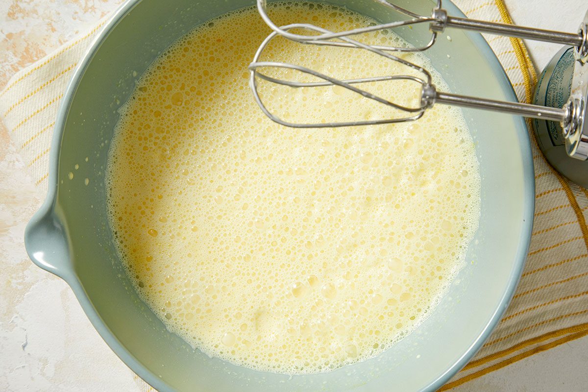 Overhead horizontal image of a batter being mixed in a blue bowl with an electric mixer. The batter is smooth and bubbly, appearing creamy in color.