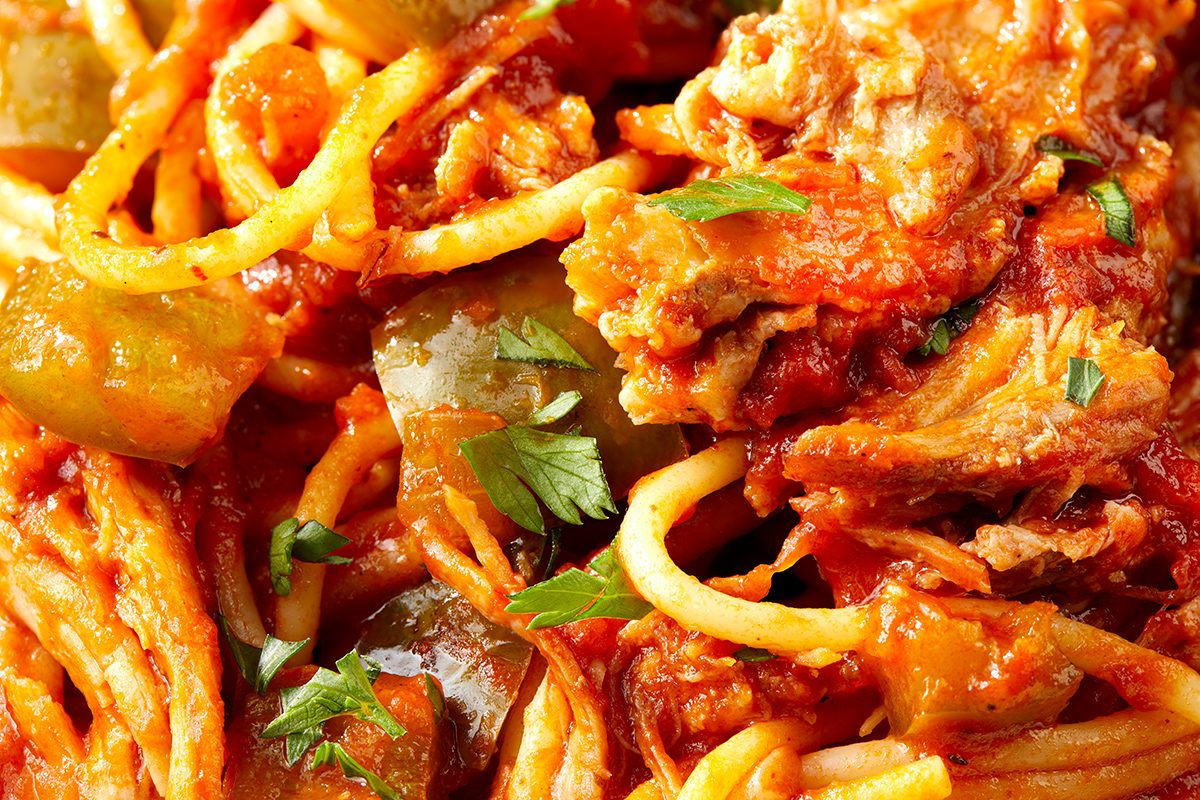 Close-up of spaghetti mixed with shredded chicken, green bell peppers, tomato sauce, and garnished with chopped parsley.