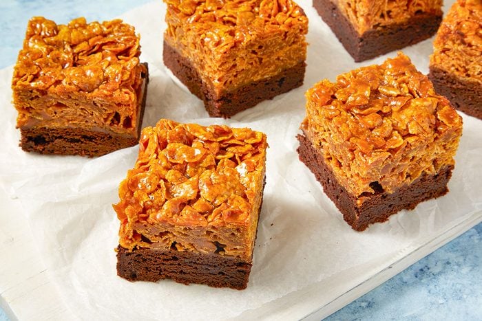 Eye Level horizontal image of cornflake brownies arranged on parchment paper. The brownies have a visible layer of caramel and are topped with cornflakes.