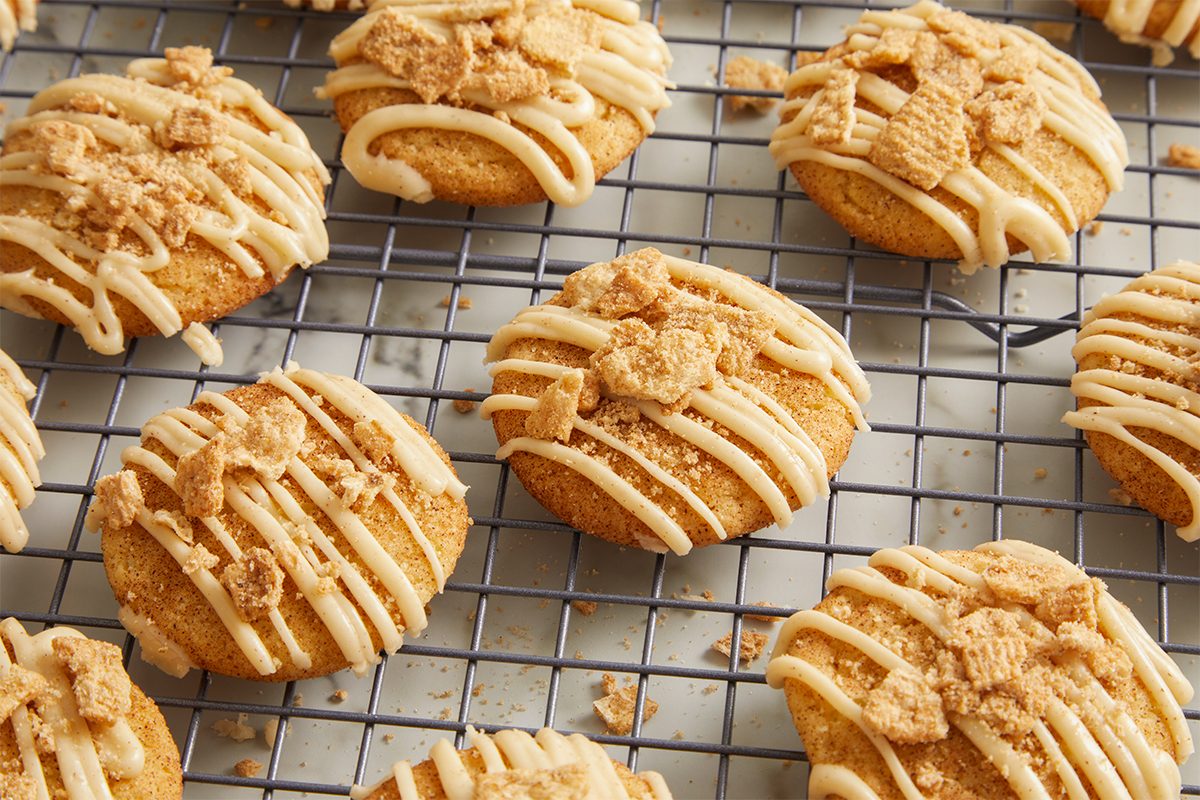 Eye Level horizontal image of a batch of frosted cookies on a wire rack. The cookies have a light brown hue and are topped with white icing and graham cracker crumbs.