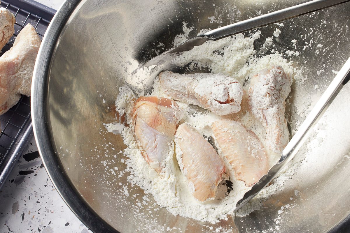 chicken wings in a large bowl being tossed and coated with cornstarch, kosher salt and baking powder mixture
