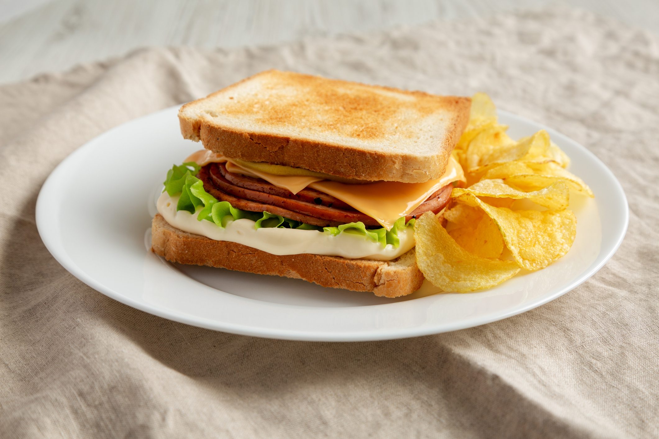 Homemade Fried Bologna and Cheese Sandwich with Chips on a Plate, low angle view.