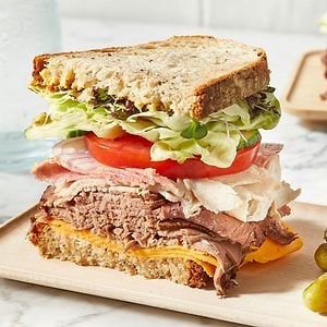 A loaded sandwich with a lot of greens, meat and cheese.