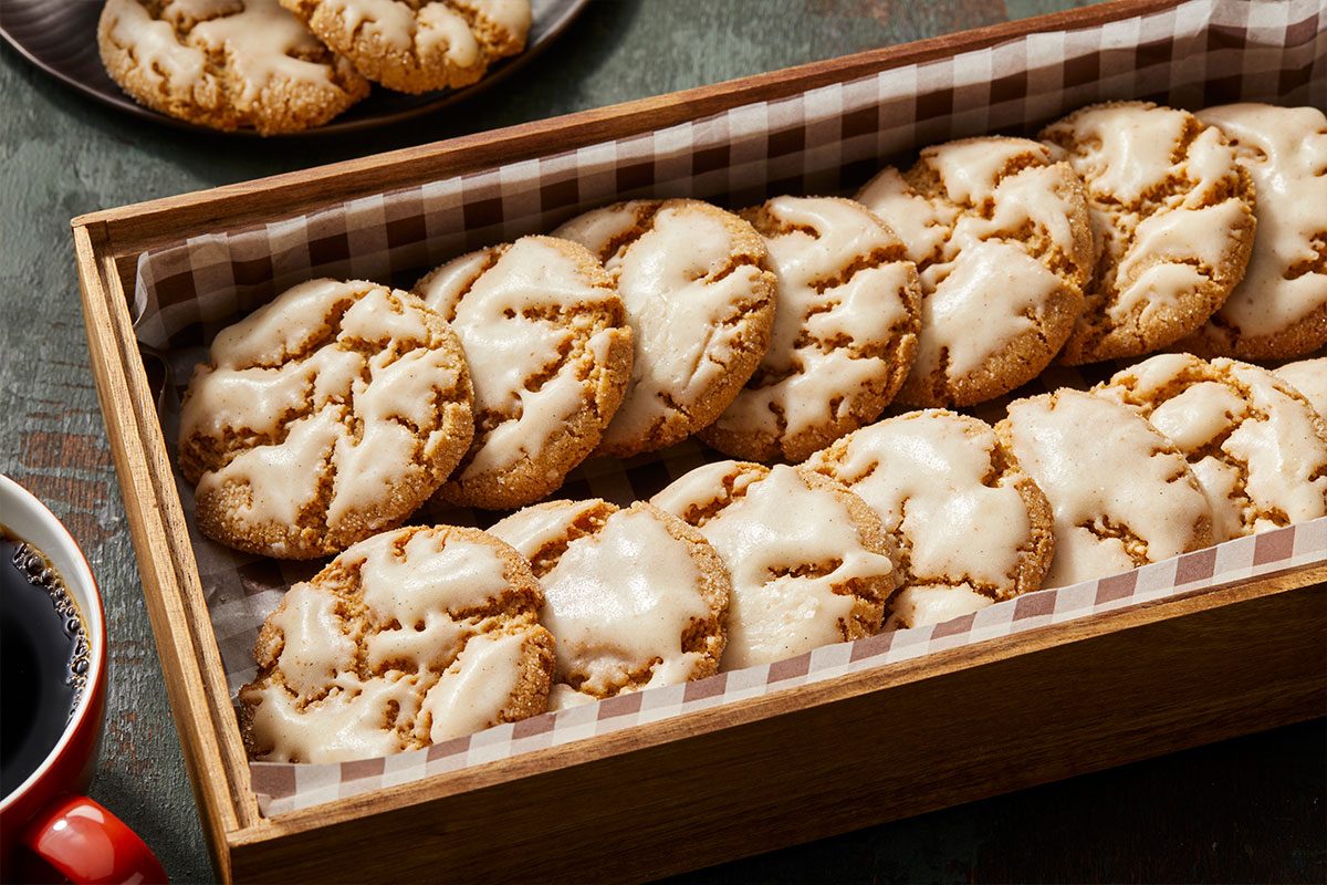 Eye Level horizontal image of iced cookies in a wooden box lined with checkered paper. Some cookies are also visible in the background and a mug of coffee appears on the left side of the frame. | [Original] RMS 281760 Iced Chestnut Cookies with Bourbon Brown Butter Icing; Horizontal AP; Pull