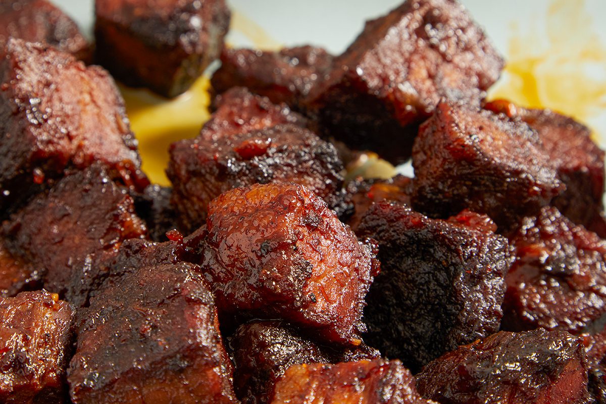 Close-up of several cubes of smoked, caramelized barbecue meat with a dark, glossy glaze, arranged closely together on a plate.