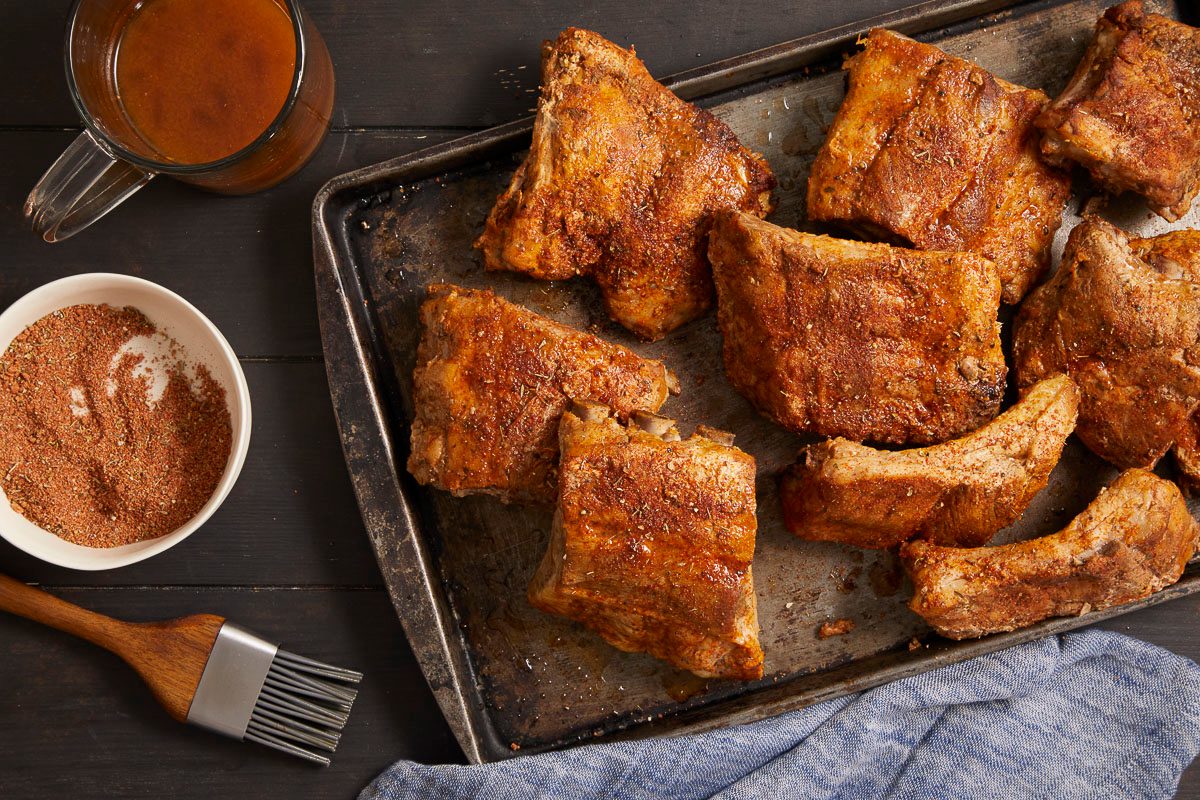 Overhead horizontal image of seasoned pork ribs arranged on a dark metal baking sheet.