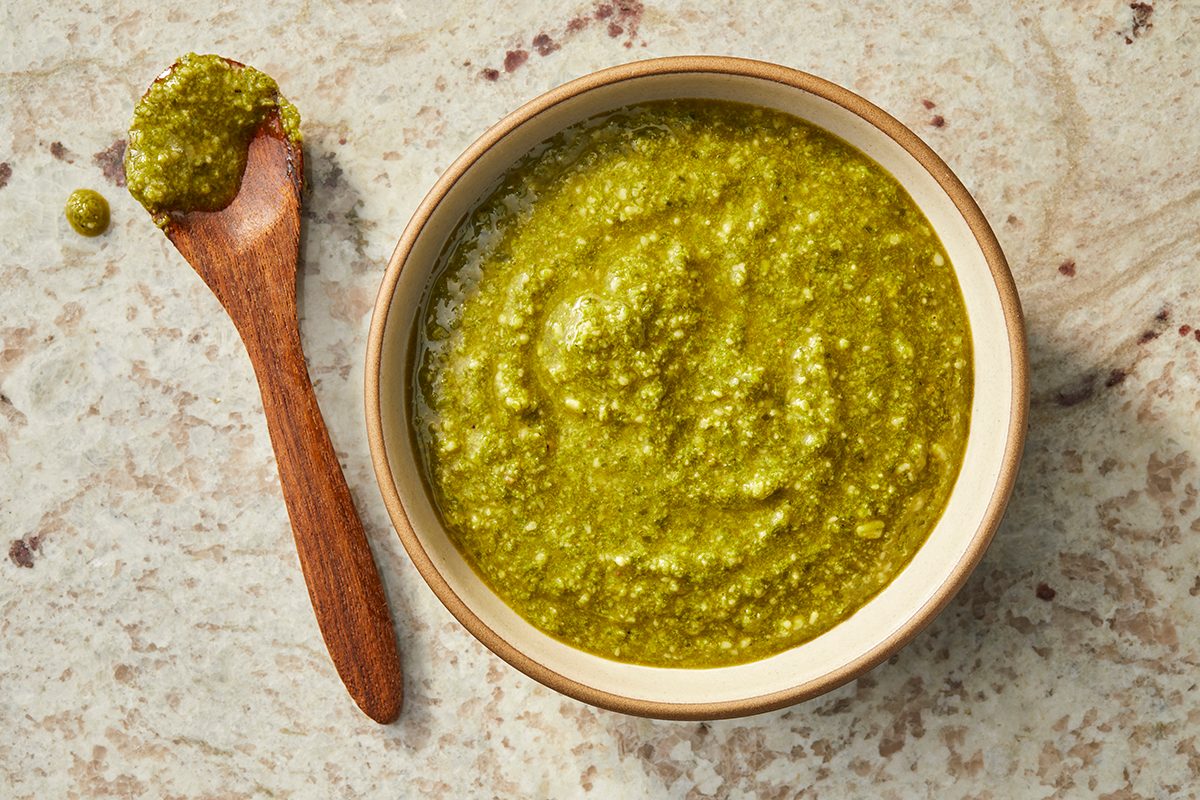 Bowl of basil pesto with a spoon showing smooth blended texture ready for serving.
