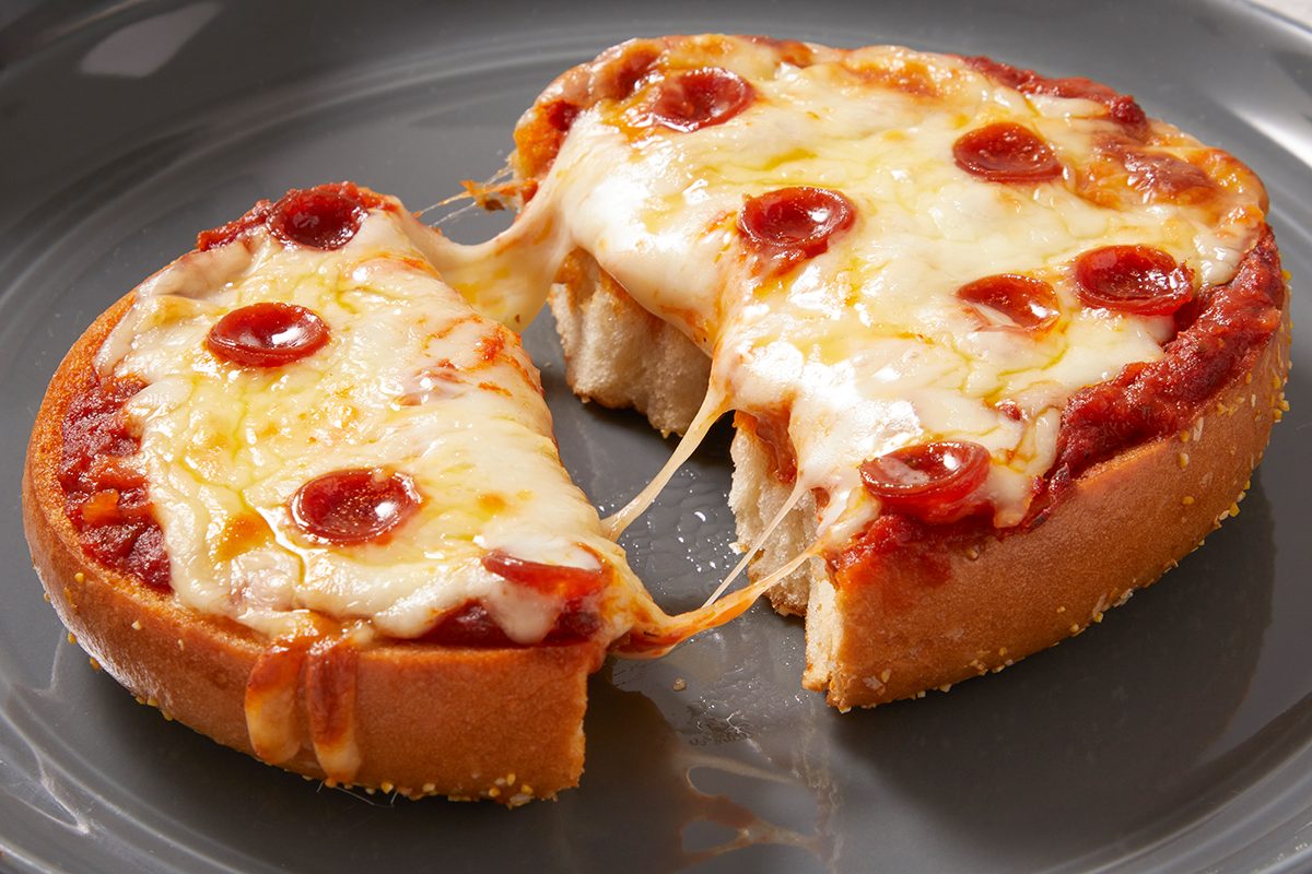 A small deep-dish pepperoni pizza with melted cheese is on a gray plate. One slice is being pulled away, showing stretchy cheese connecting it to the rest of the pizza.