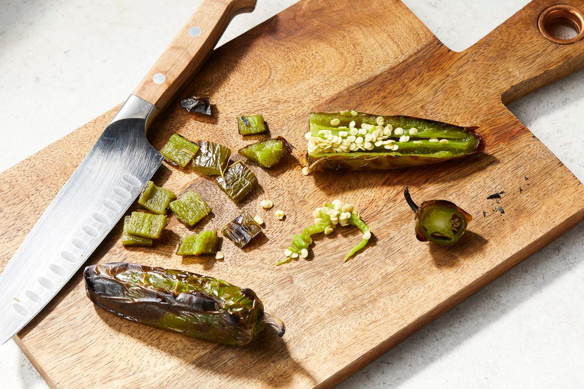 sliced charred jalapeno on a cutting board next to a knife