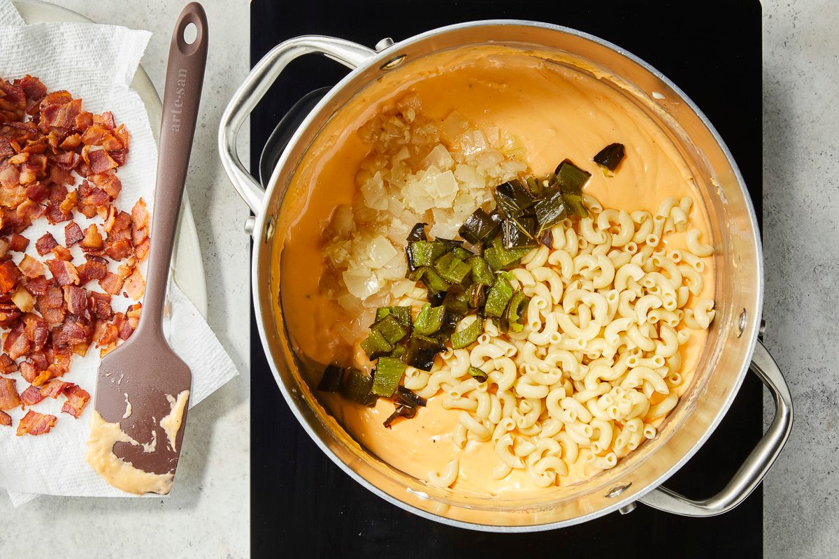 Overhead image of a pot containing a creamy orange cheese sauce with cooked macaroni pasta, diced onions, and chopped green peppers.