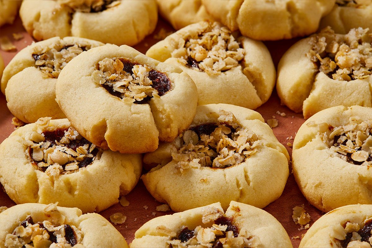 Eye Level horizontal image of thumbprint cookies filled with jam and topped with chopped nuts. The golden brown cookies are arranged close together. | [Original] RMS 281597; Sugar Plum Thumbprint Cookies; Horizontal Push