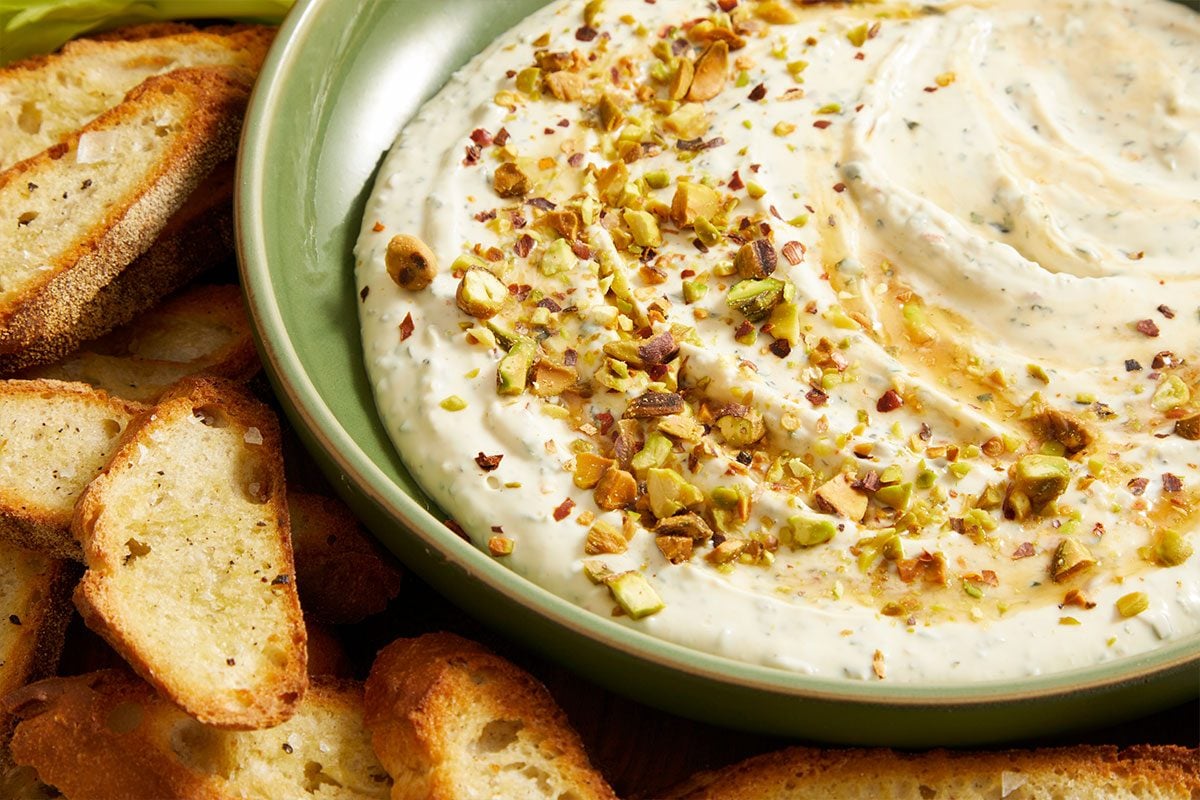 A bowl of hummus accompanied by bread, all presented on a vibrant green plate.