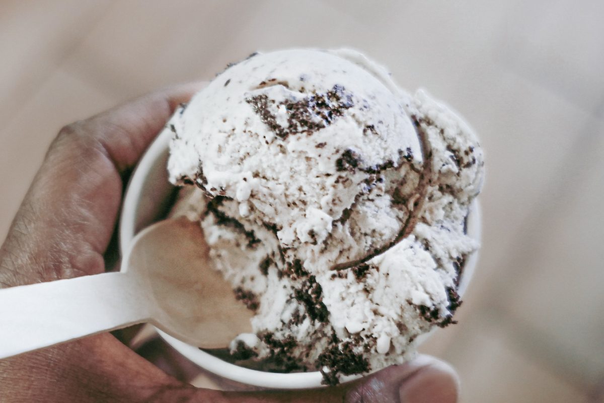 close up of a hand holding Wolf Tracks Ice Cream in a paper cup with a spoon