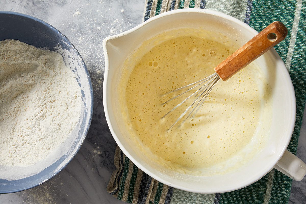 Overhead horizontal image of egg yolk batter being whisked with flour and buttermilk for Danish aebleskivers.