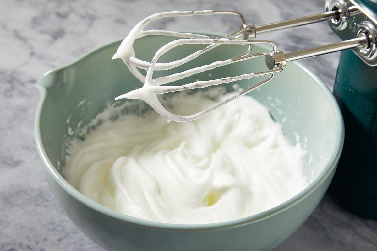 Overhead horizontal image of egg whites being whipped to soft peaks for incorporation into batter.