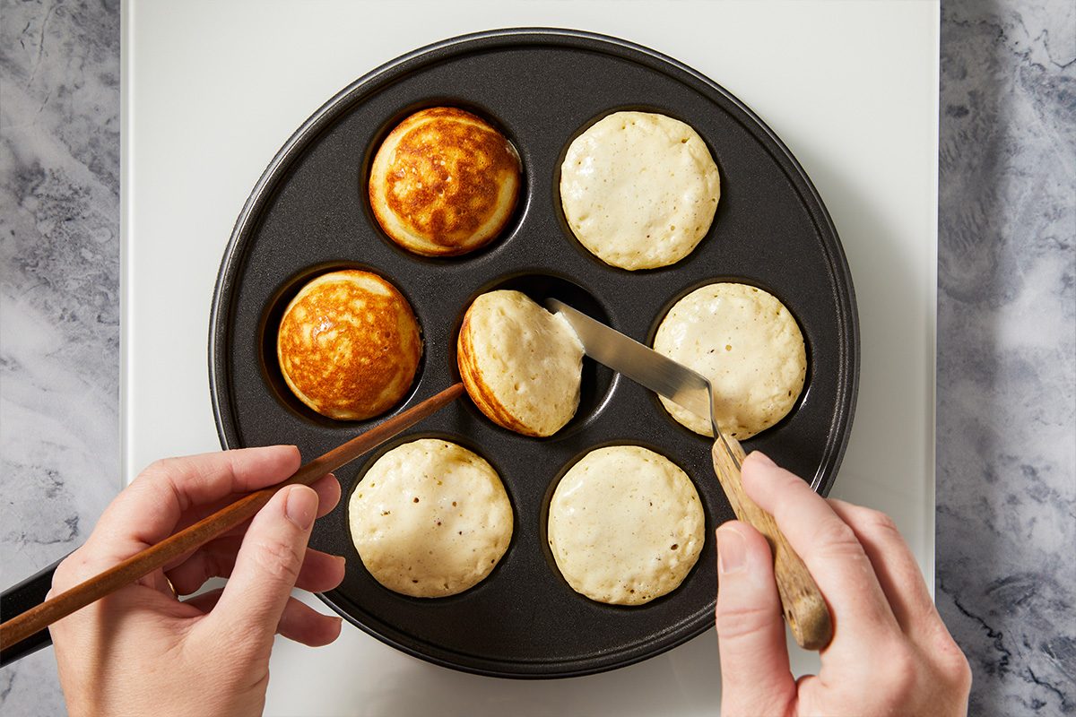 Overhead horizontal image of batter cooking in an aebleskiver pan while being turned to form round pancakes.