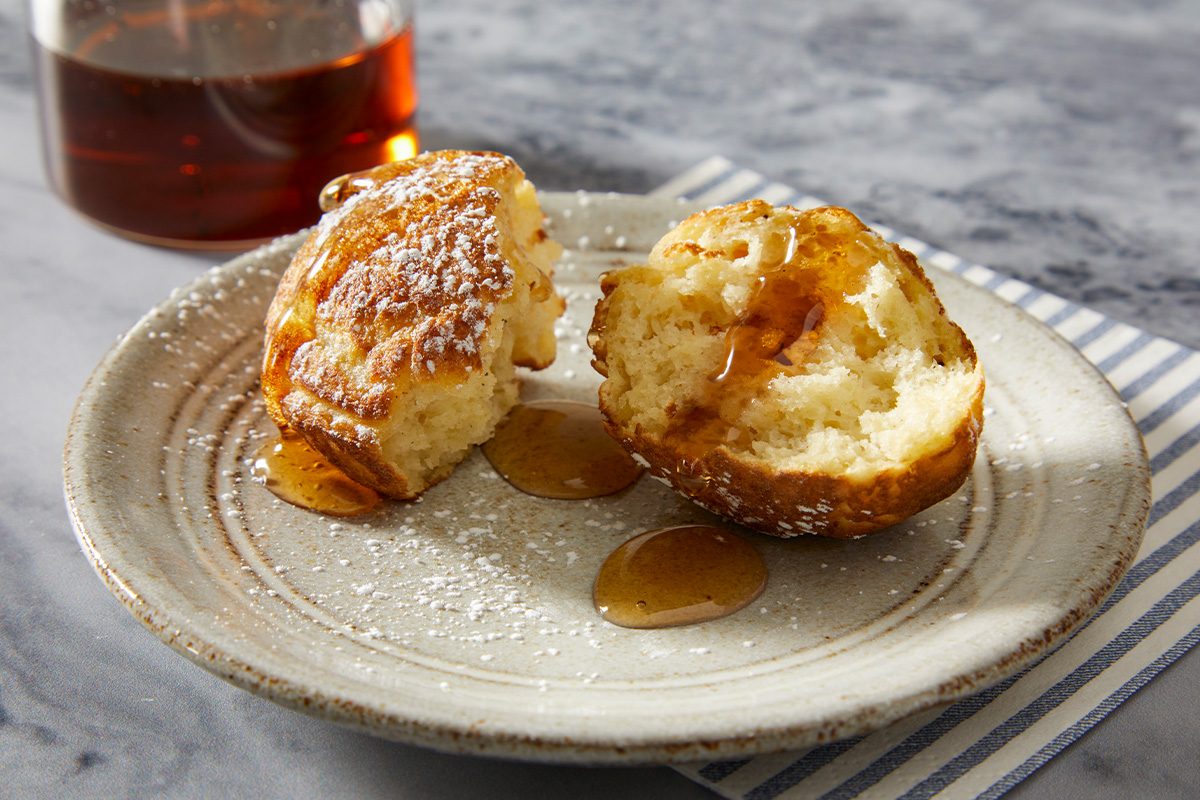 Eye-level horizontal image of aebleskivers served with maple syrup and a split interior showing soft texture.