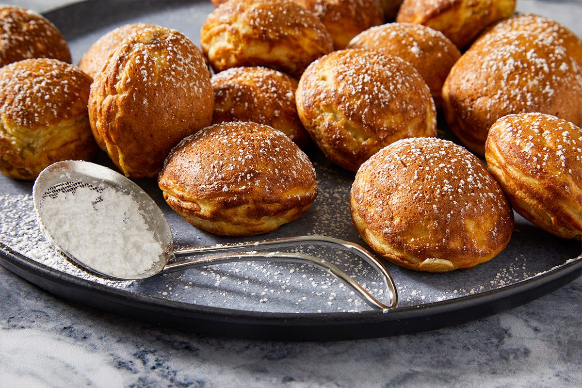 Eye-level horizontal image of aebleskivers arranged on a platter dusted with powdered sugar.