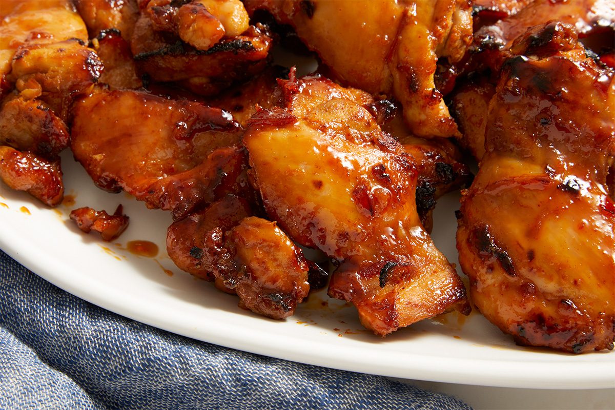 Close-up shot of Copycat Cava Harissa Honey Chicken with a glossy caramelized coating and lightly charred edges; highlighting the sticky glaze and juicy texture on a white serving platter;