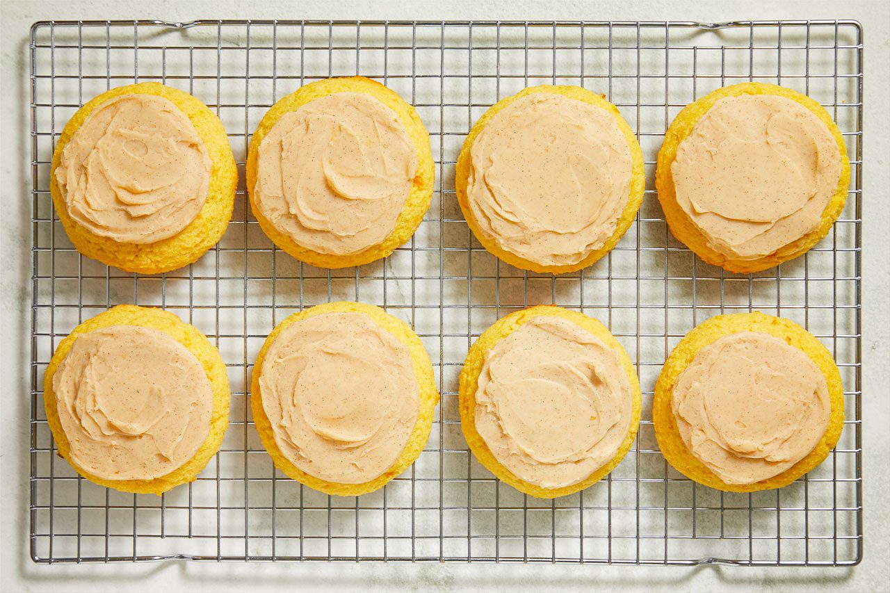 Overhead shot of frosted corn cookies arranged on a wire cooling rack, each topped with a smooth swirl of creamy frosting;