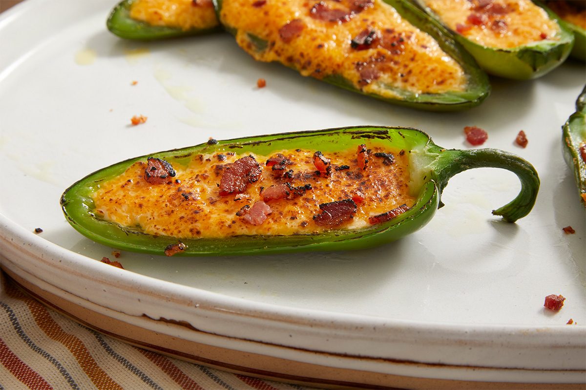 Close-up shot of a Easy Cheese-Stuffed Jalapeños on a white plate, showcasing the crispy bacon bits and bubbly cheese filling.