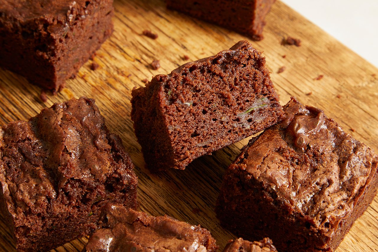 Several rich, fudgy chocolate brownies are arranged on a wooden cutting board, with a close-up view highlighting their moist, dense texture and slightly crispy tops.