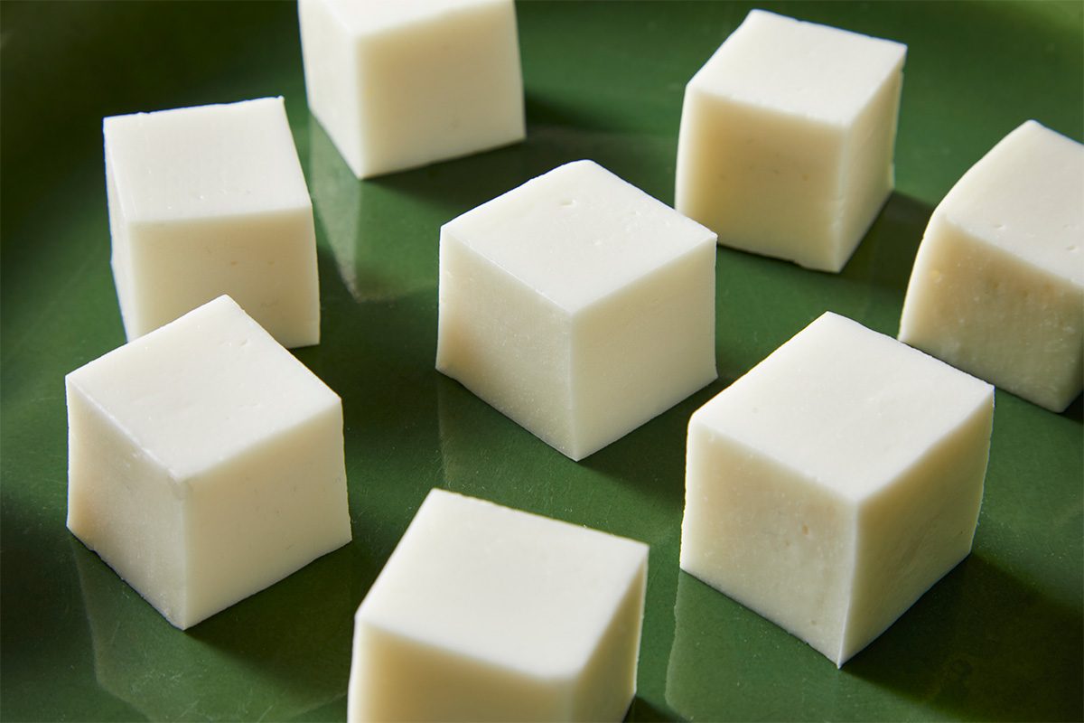 Close-up shot of smooth, creamy haupia cubes arranged on a glossy green platter, highlighting their silky texture;