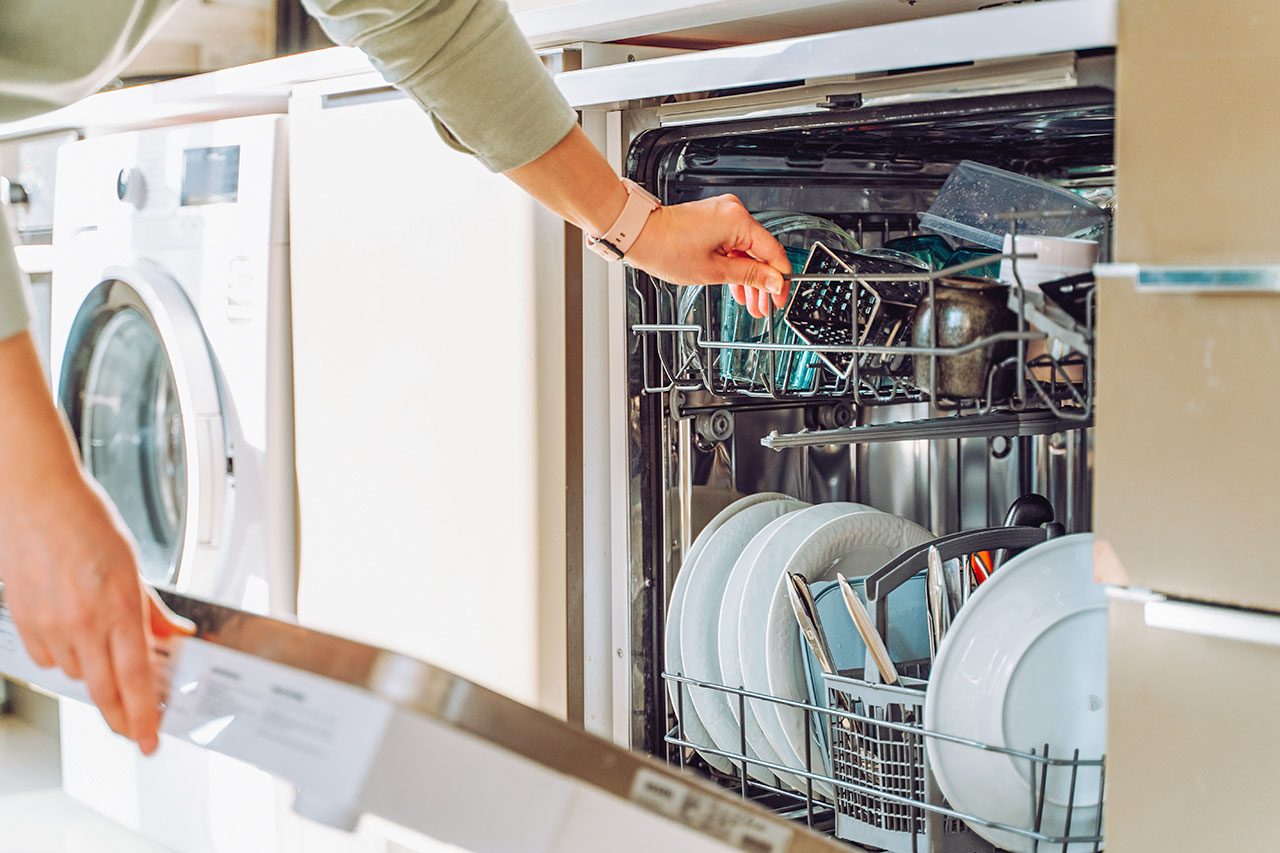 Close up cropped hands loading dish washing machine near washing machine in modern built in kitchen