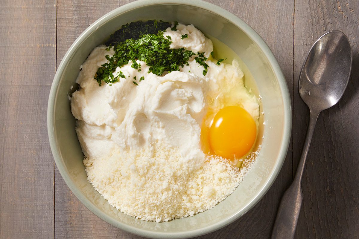 Overhead step-by-step food photography showing ricotta cheese, egg, Romano cheese, and parsley combined in a bowl to create manicotti filling.