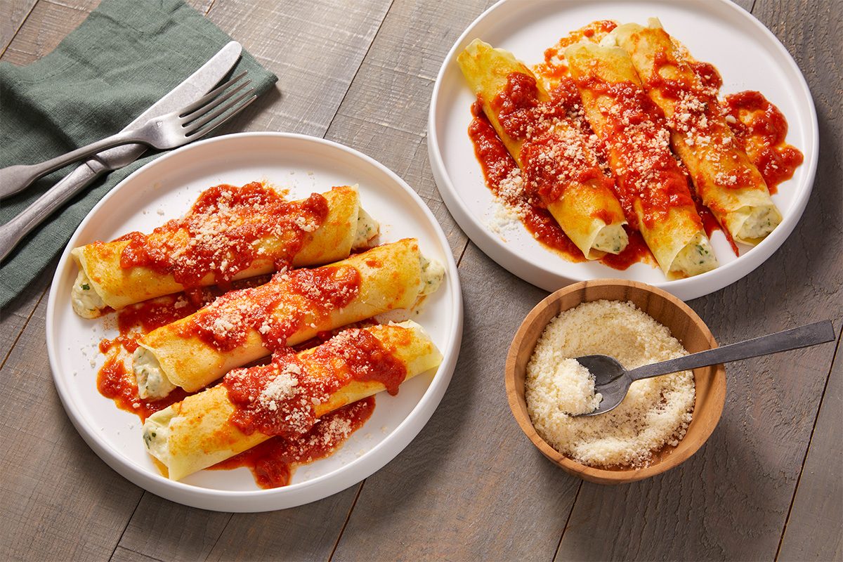 Overhead food photography showing Homemade Manicotti plated and served with marinara sauce and grated cheese.