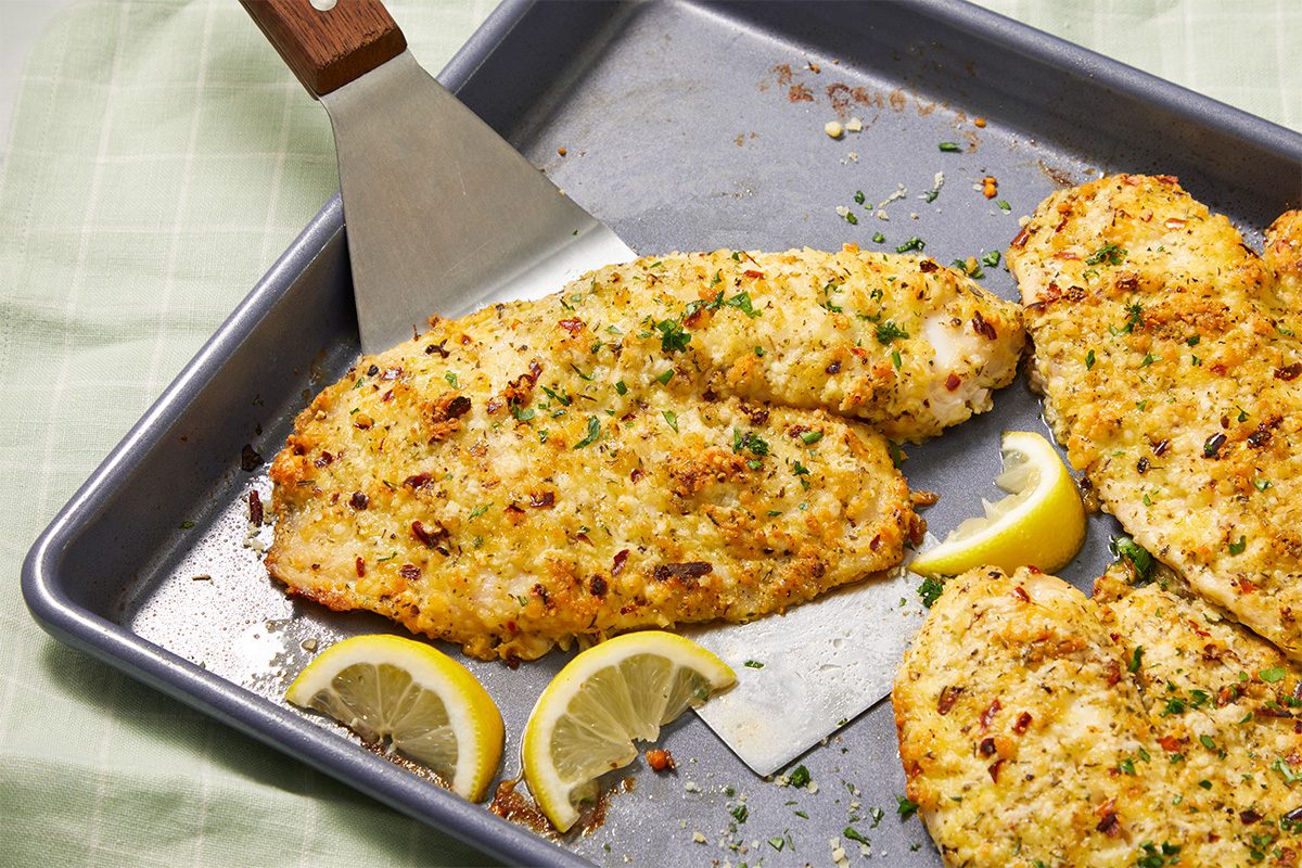A horizontal image shows a spatula lifting a baked tilapia fillet from a sheet pan, with lemon wedges and seasoning visible.