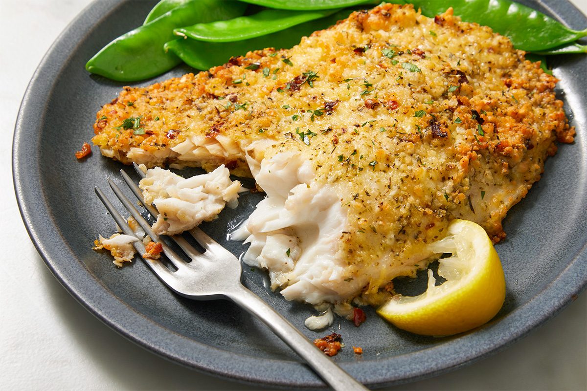 A horizontal image shows a spatula lifting a baked tilapia fillet from a sheet pan, with lemon wedges and seasoning visible.