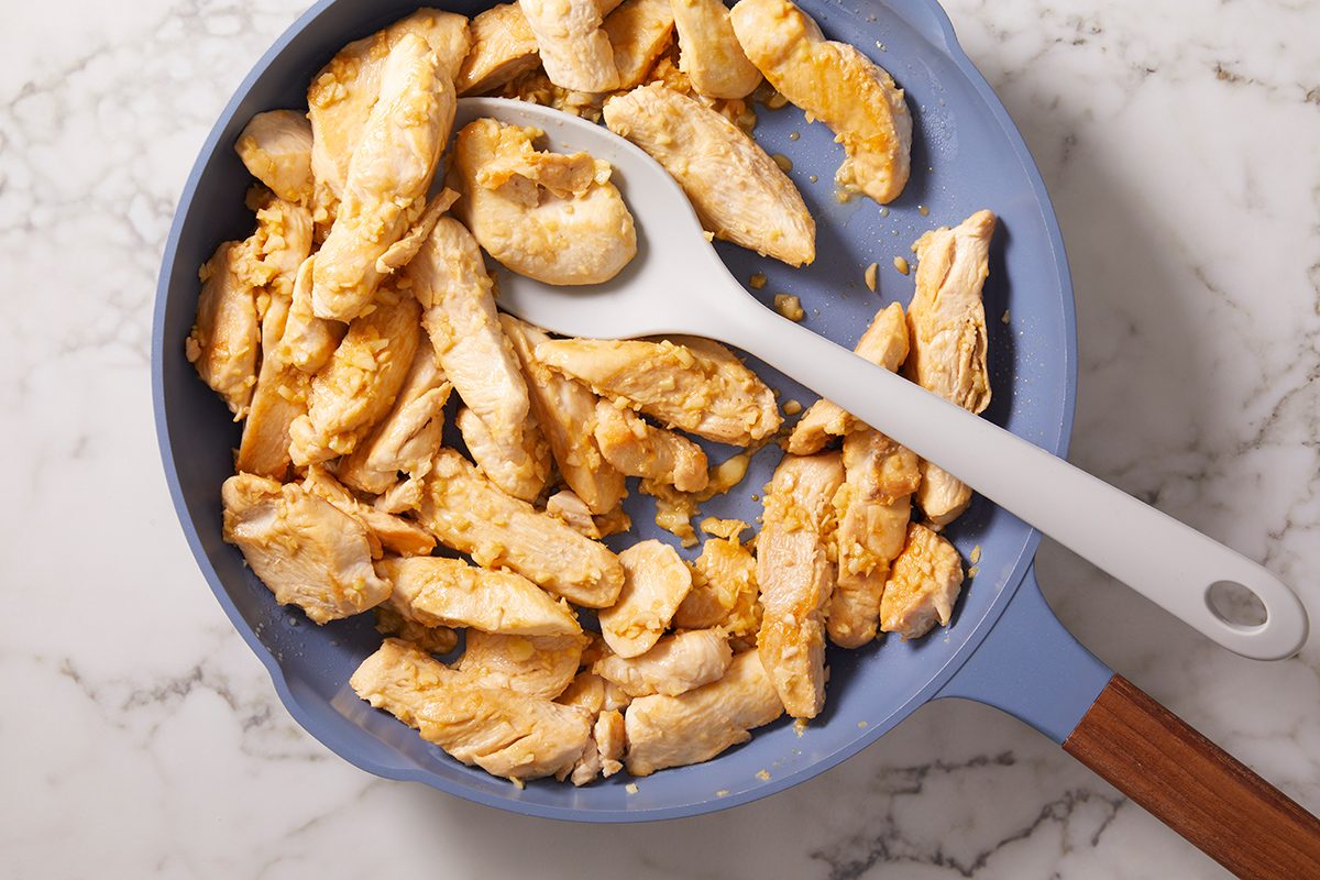 Cooked chicken strips in a blue skillet with a white and gray spatula, sitting on a marble countertop.