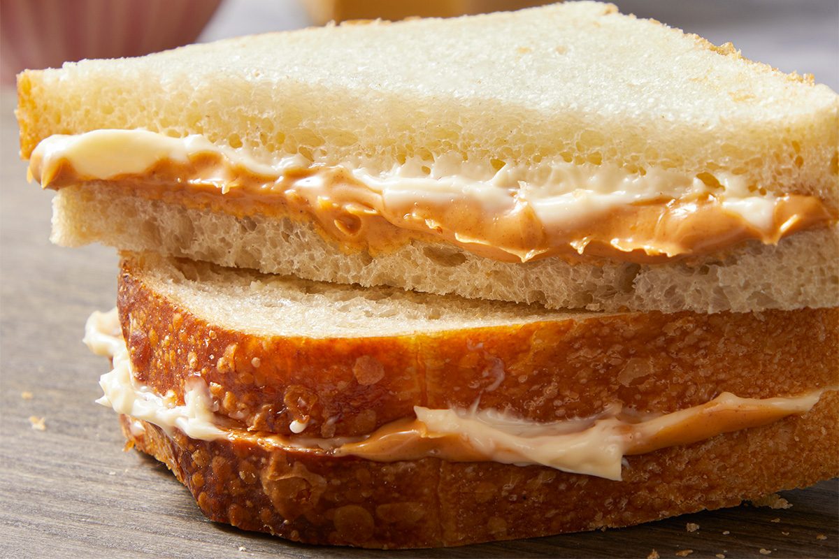 Eye Level horizontal image of a sandwich made with white bread, peanut butter, and mayonnaise, cut in half and stacked. The creamy peanut butter and white mayonnaise are visible between the layers of bread, which includes a lightly toasted bottom slice.