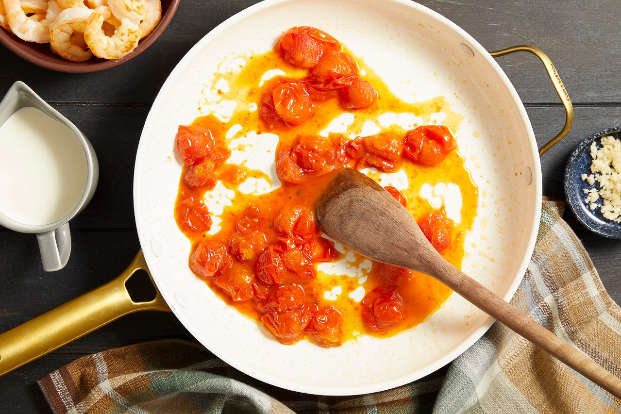 Overhead shot of cherry tomatoes simmering in a creamy saffron sauce in a white skillet