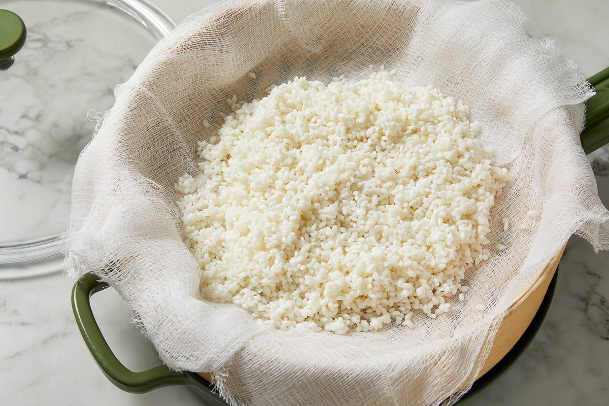 Overhead horizontal image of white short-grain rice piled inside a cheesecloth-lined green pot.