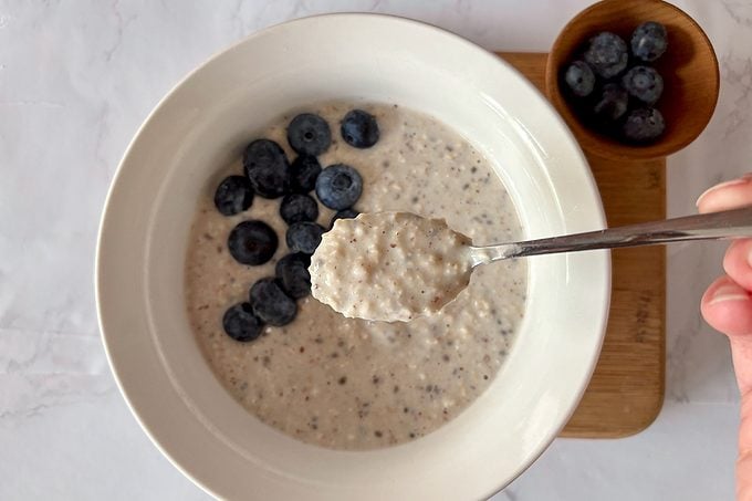 close up of oatmeal on a spoon with a bowl containing more oatmeal and blueberries in the background