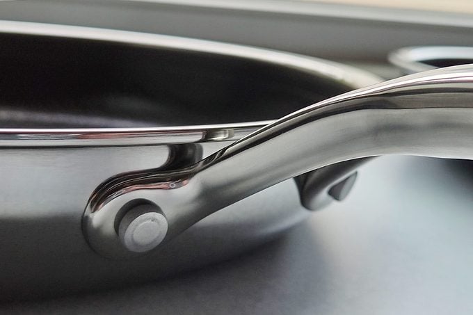 Close-up view of a stainless steel frying pan handle attached to the side of the pan, resting on a smooth gray surface.
